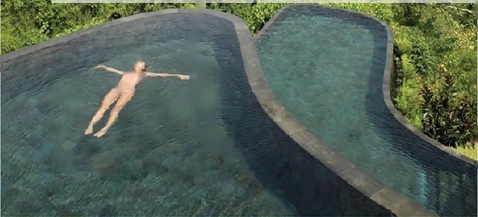 Zero-edge infinity pool resting on the jungle canopy with a guest floating