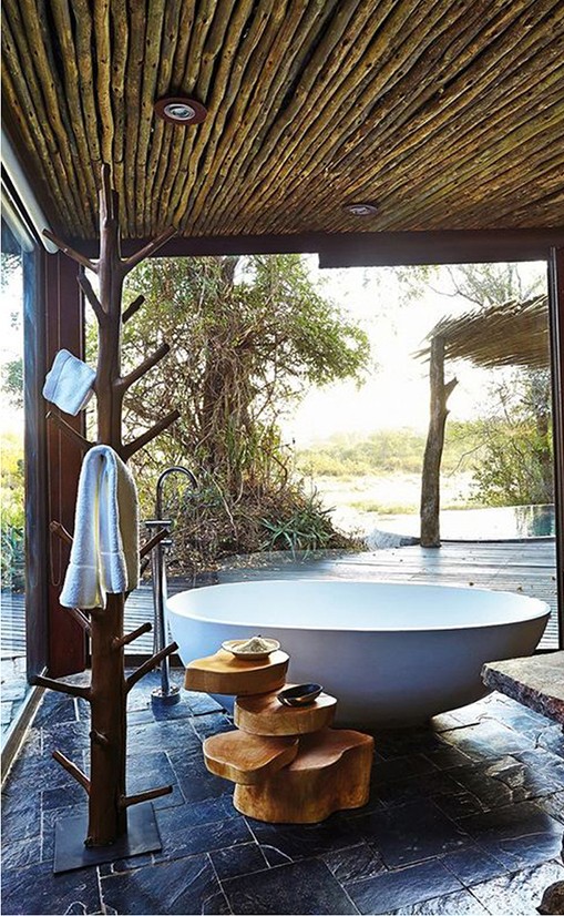 Freestanding stone bathtub in an open-air bathroom with bamboo ceiling and jungle views